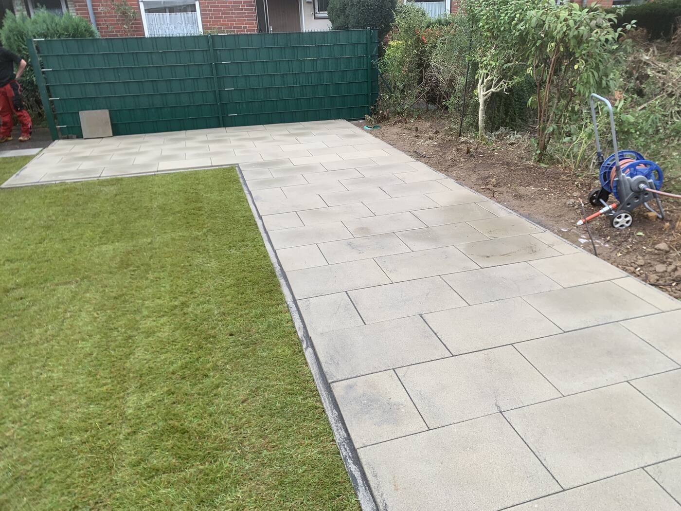 Terrasse mit hellen Platten und frischem Rollrasen